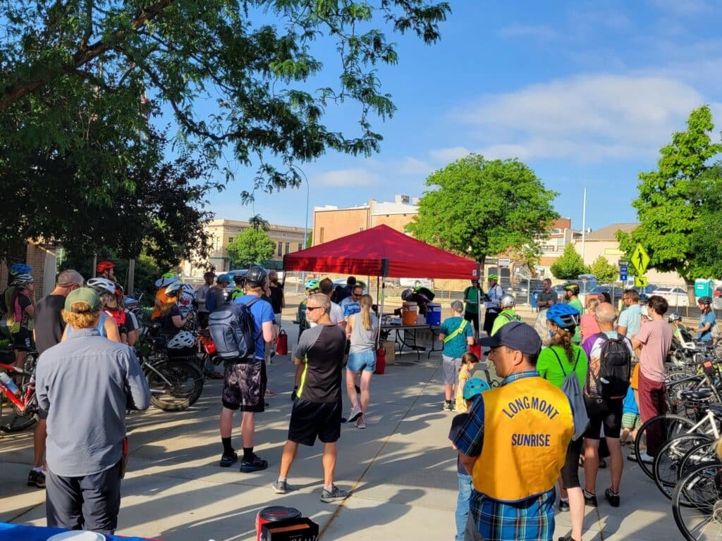 Cyclists gather under a red tent for Bike to Work Day Longmont at Civic Center Plaza, enjoying pancakes, raffles, and community booths.