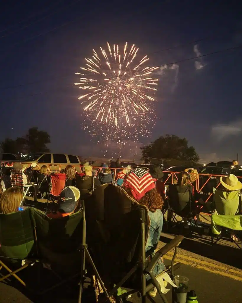 Longmont 4th of July Street Party Set to Light Up Downtown Crowd seated in lawn chairs watching a fireworks display during the Longmont 4th of July street party at night.