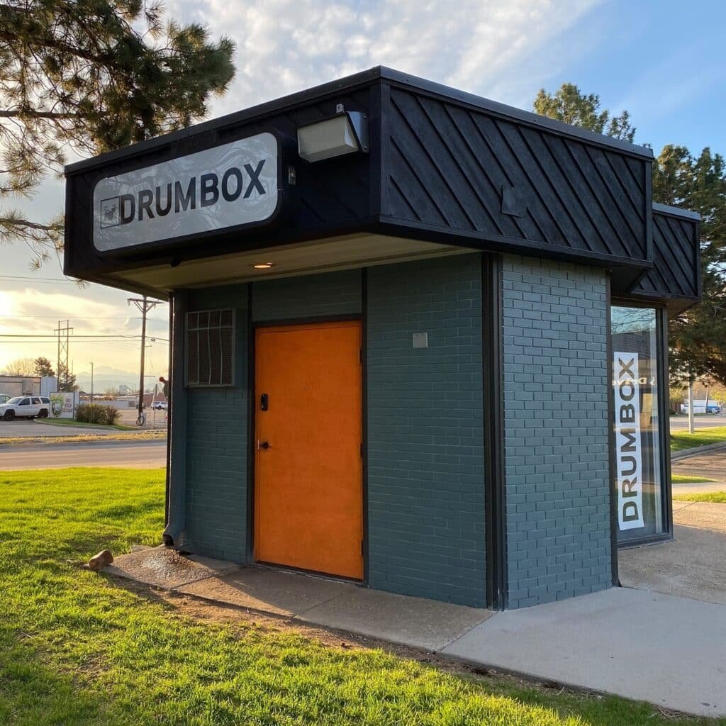Drum Box Longmont: Inclusive, Soundproof Studio for Drummers & Bands Exterior view of Drum Box Longmont, a modern standalone rehearsal studio with a bold orange door and prominent signage.
