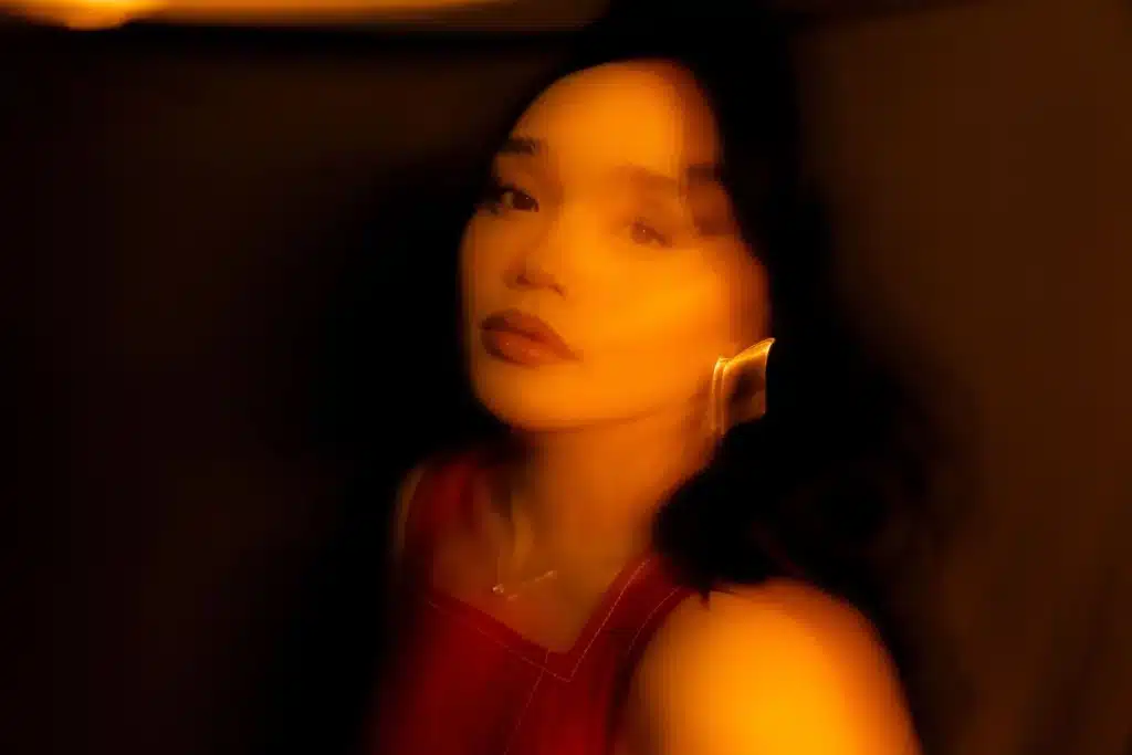 Indie 102.3 Local 303: Discover July 2025's Featured Colorado Artists Portrait of musician Hunnie, a Colorado Public Radio artist, in warm, blurred lighting, wearing a red top and a distinctive gold earring