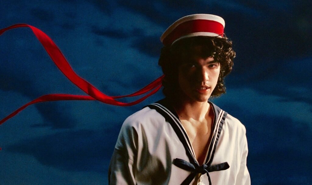 Conan Gray wearing a sailor-inspired outfit with a red ribbon hat, featured in promotional imagery for his album Wishbone.