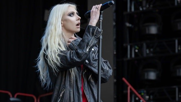 Taylor Momsen of The Pretty Reckless performing live on stage, holding a microphone and wearing a black leather jacket.