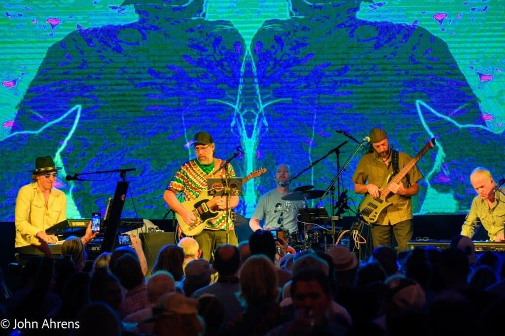Steely Dead performing live at Wibby Brewing Festgarten, August 16, 2025, with vibrant psychedelic backdrop – photo by John Ahrens.