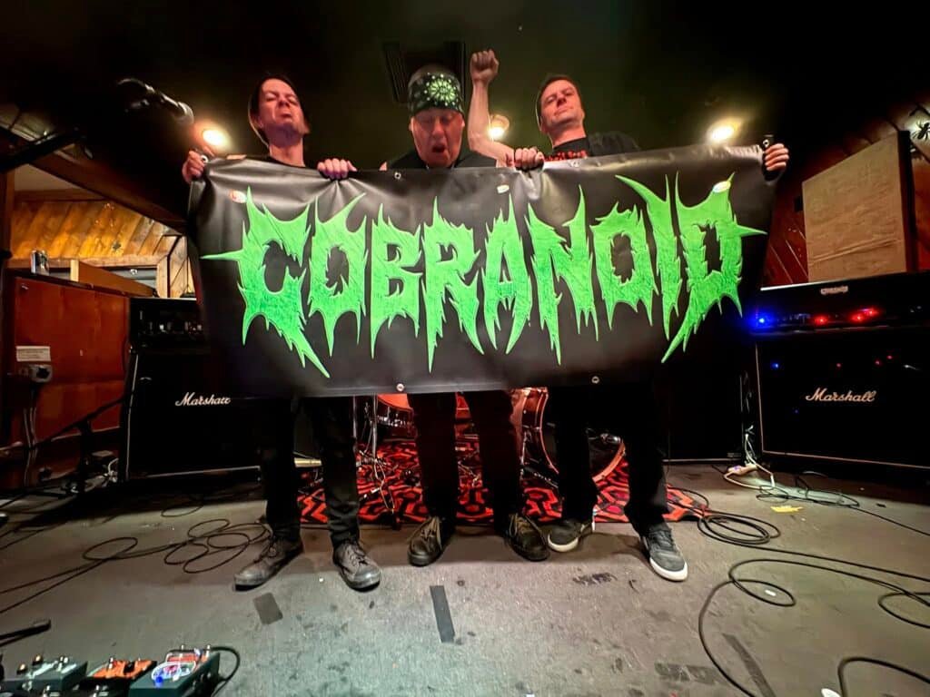 Cobranoid Denver metal band holding banner on stage with Marshall amps in the background