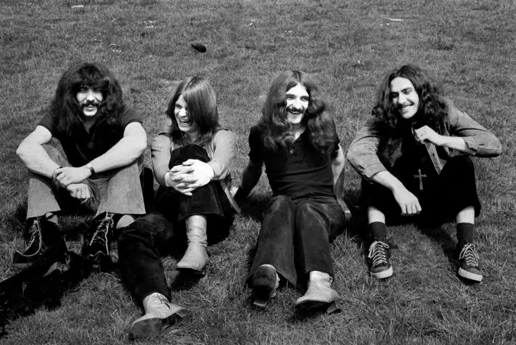 The original Black Sabbath Debut Album lineup sitting together outdoors in 1970, featuring the members laughing and relaxed on the grass.