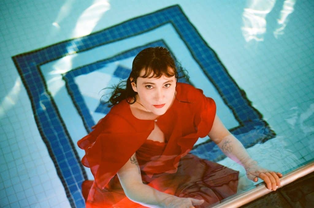 Claire Heywood in a red dress submerged in water, promoting her 2025 debut album Claire Heywood Water Is All I See
