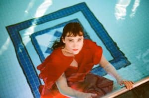 Claire Heywood in a red dress submerged in water, promoting her 2025 debut album Claire Heywood Water Is All I See