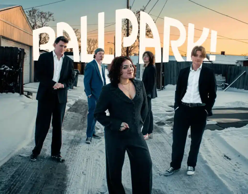 The Ballpark Band Denver members posing in suits in a snowy alleyway with their logo in the background.