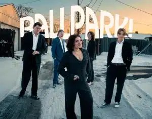 The Ballpark Band Denver members posing in suits in a snowy alleyway with their logo in the background.
