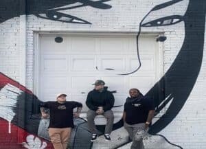 Members of Hailes Ghost Denver punk band standing in front of a black-and-white street art mural in Denver