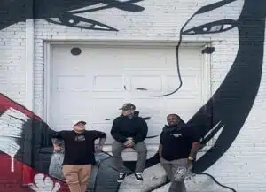 Members of Hailes Ghost Denver punk band standing in front of a black-and-white street art mural in Denver